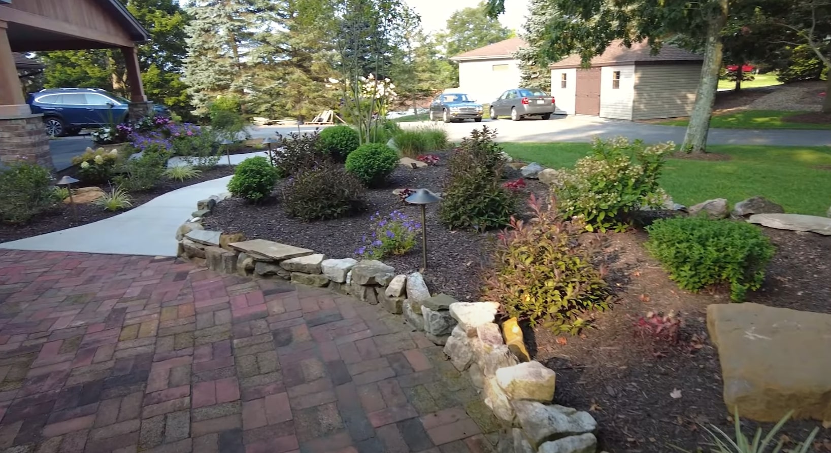 Complete Landscape Installation Professional landscape installation with decorative stone elements, colorful plantings, and brick paver patio